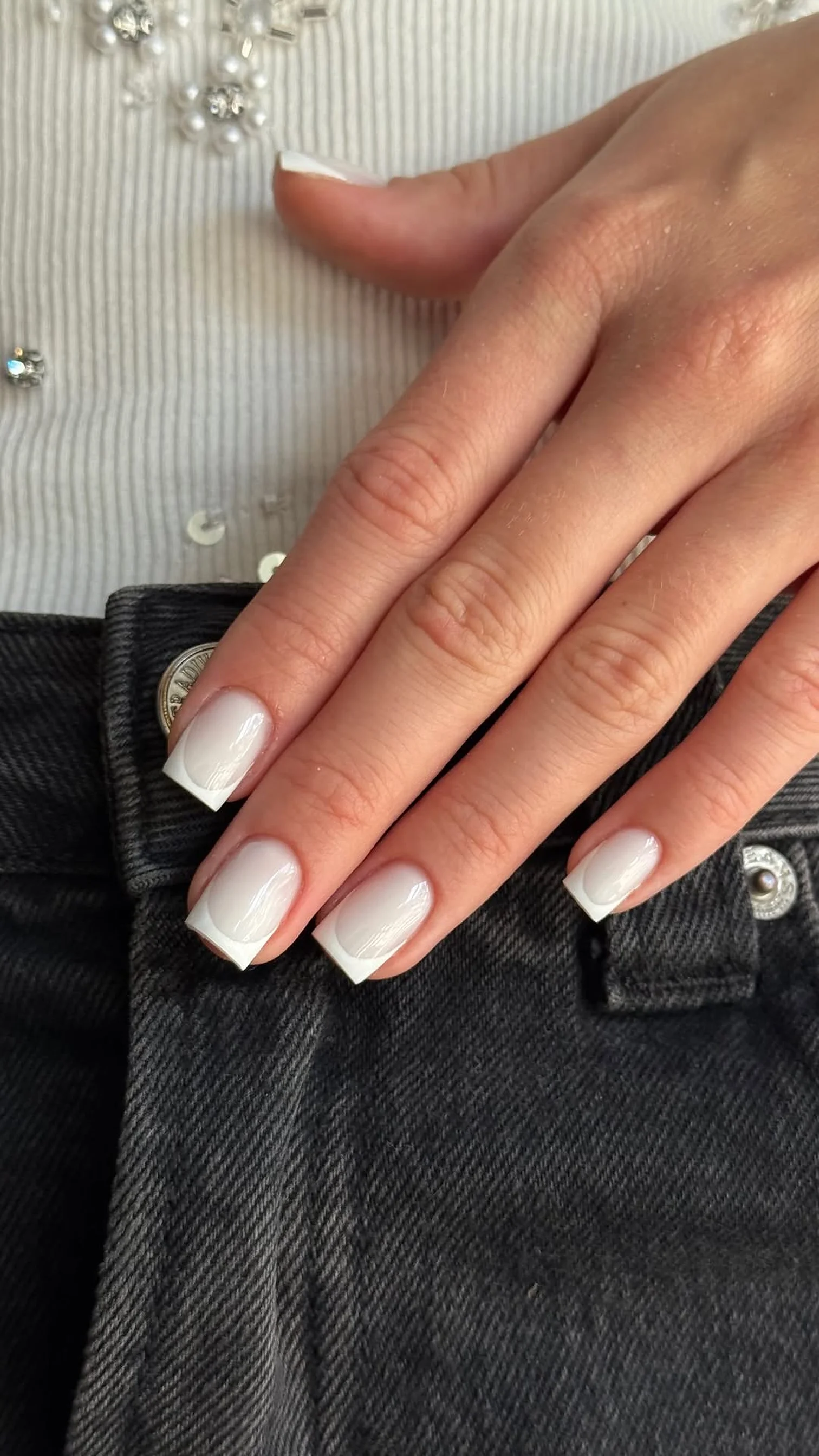 Short milky white nails against black jeans